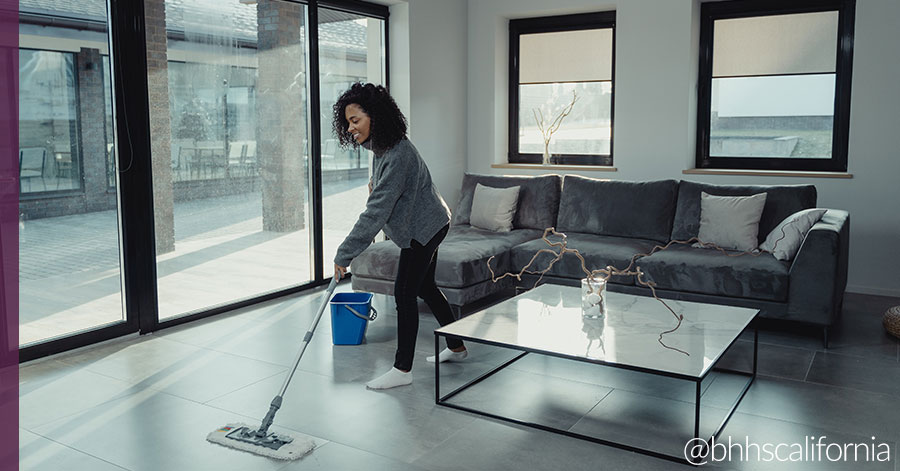 young woman mopping floor of her modern home with glass walls using a mop, bucket, and diy floor cleaner.