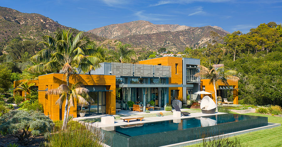 luxury home with yellow exterior and endless pool with mountains in background.