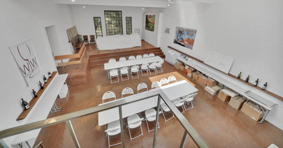 Large gallery with windows and high ceilings featuring tables, a stage, and wine tasting areas