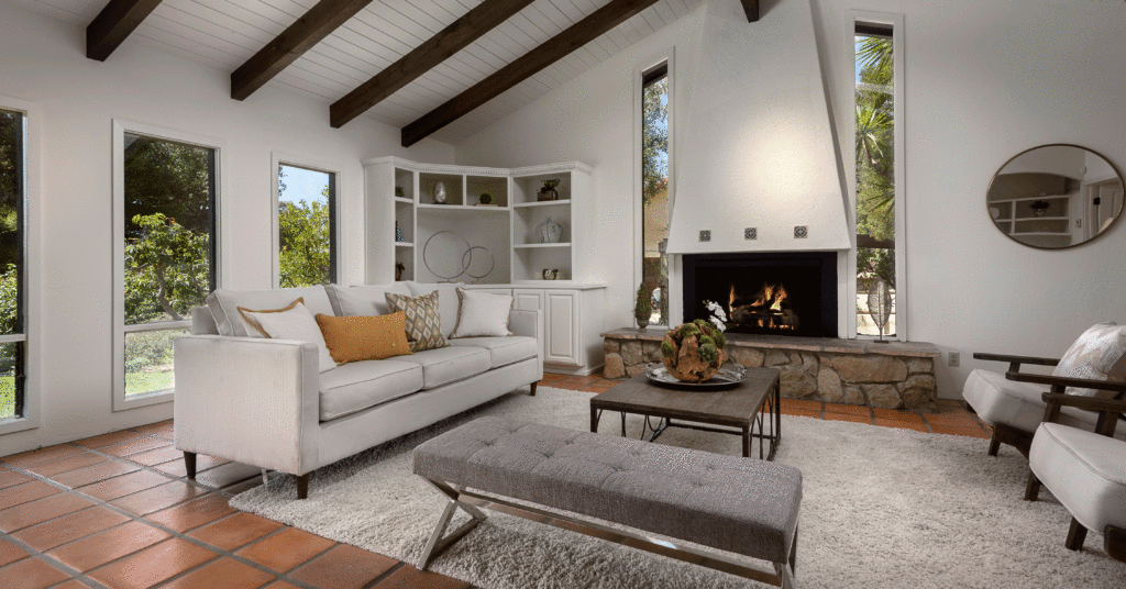 All white living room with prominent fireplace and dark beamed ceilings. 