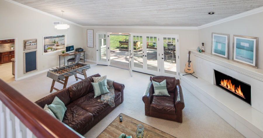 Aerial view of living room with seating area, foosball table, and doors that are open to patio outside.