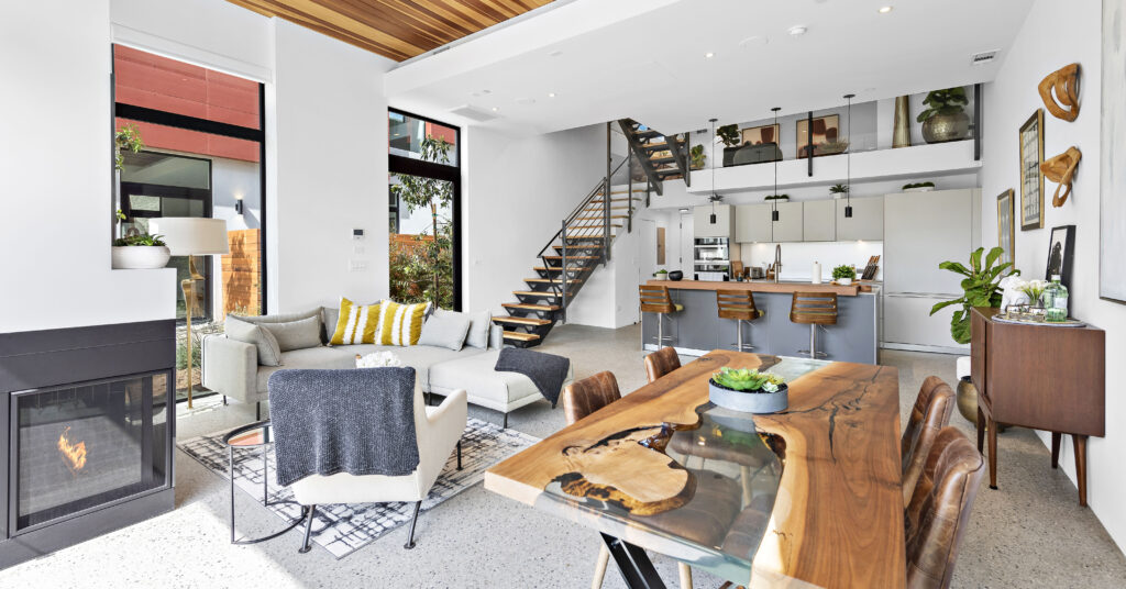 Modern eclectic living room with kitchen and staircase in background. 