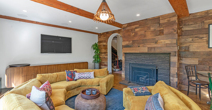 Living room with circlular yellow couch and fireplace on an all wood paneled wall 