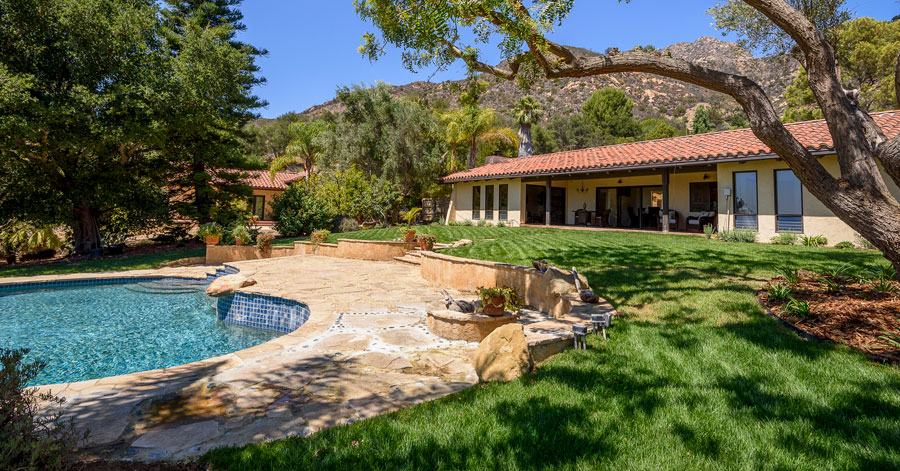 One story home with green grass and pool and mountains in the background