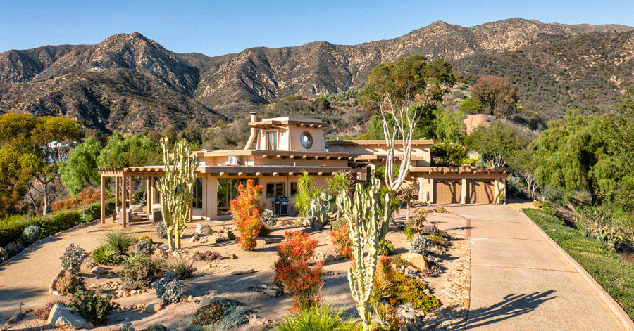 Long driveway leads past drought tolerant landscaping to luxury home with mountains in the background 