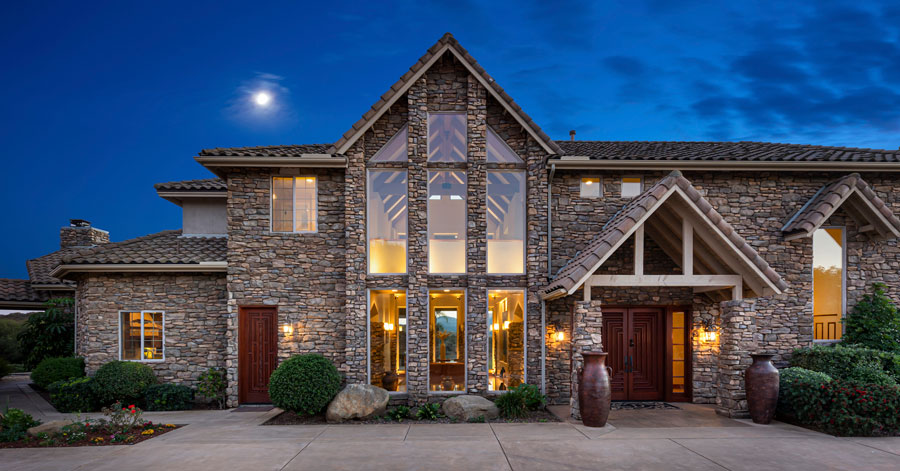 Luxury home with stone exterior and large windows at dusk 