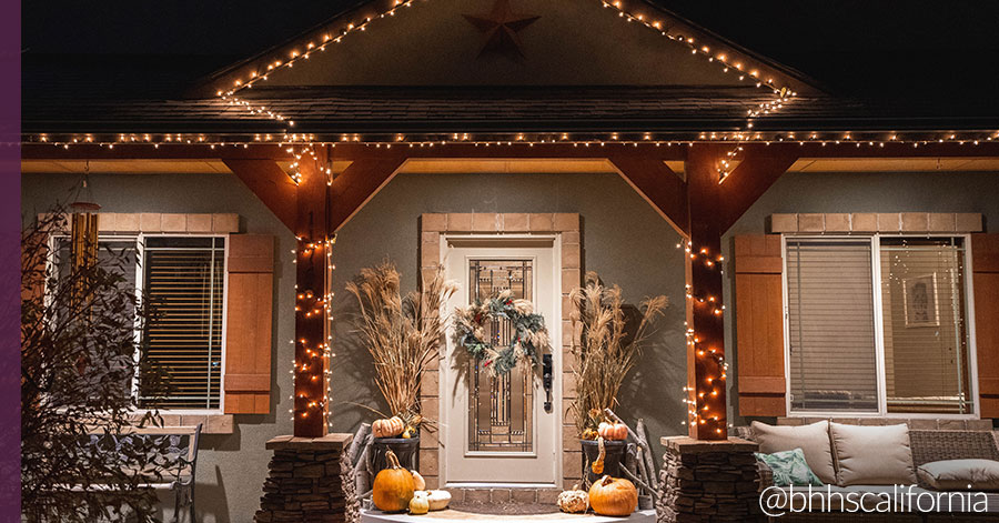 Exterior of home with holiday decorating with string lights, pumpkins, and a wreath on the front porch. 