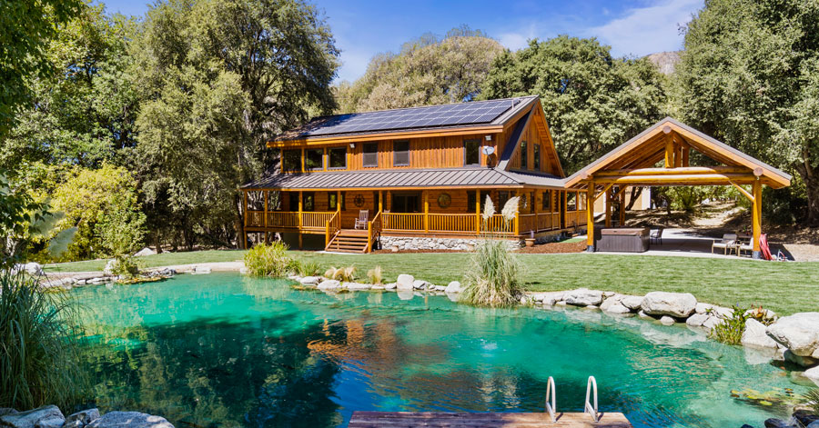 Two story cabin with light brown wood behind a peaceful spring fed pool surrounded by rocks and plants