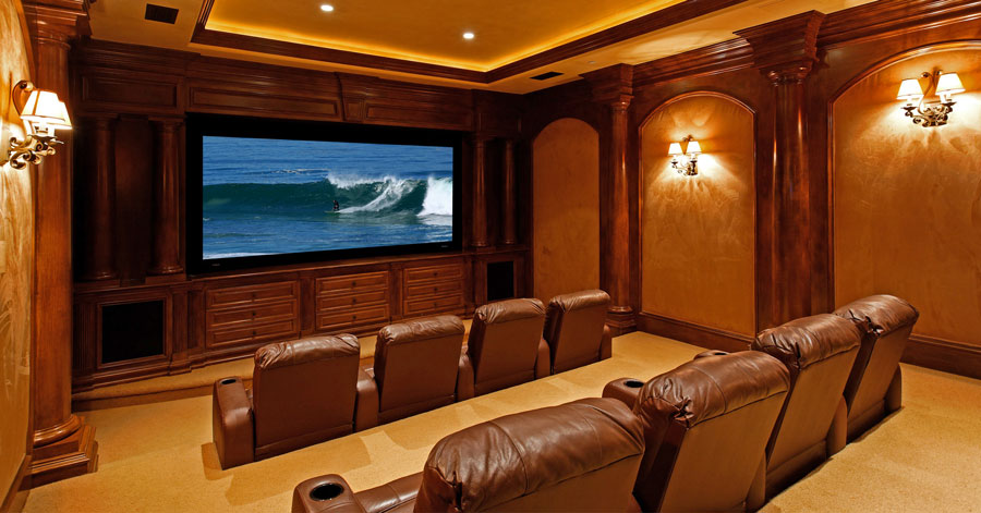 Large movie screen in a room with dark brown wood wall paneling and brown leather theater seats. 