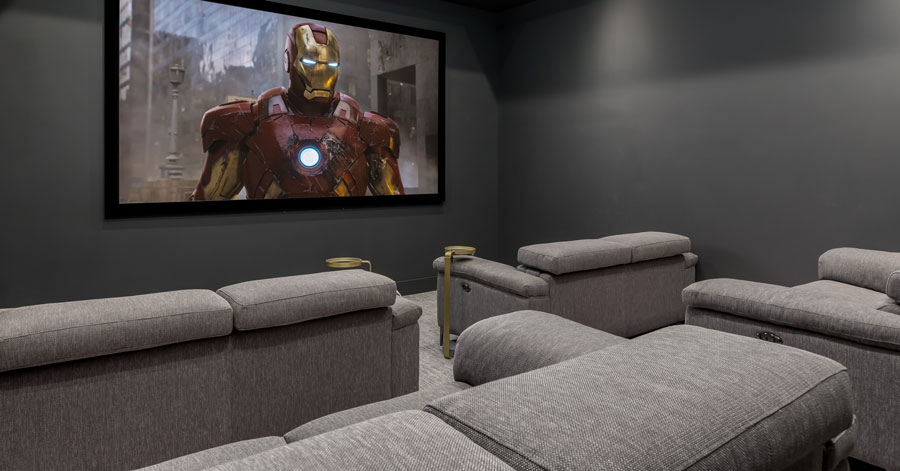 Dark grey walls and light grey couches with a large movie screen. 