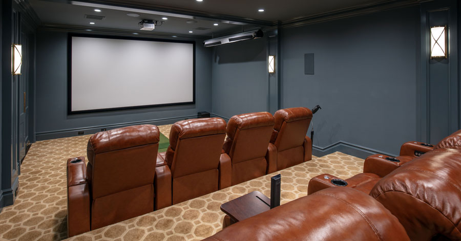 Home theater with large screen, dark grey-blue walls, brown leather seats, an tan patterned carpet. 