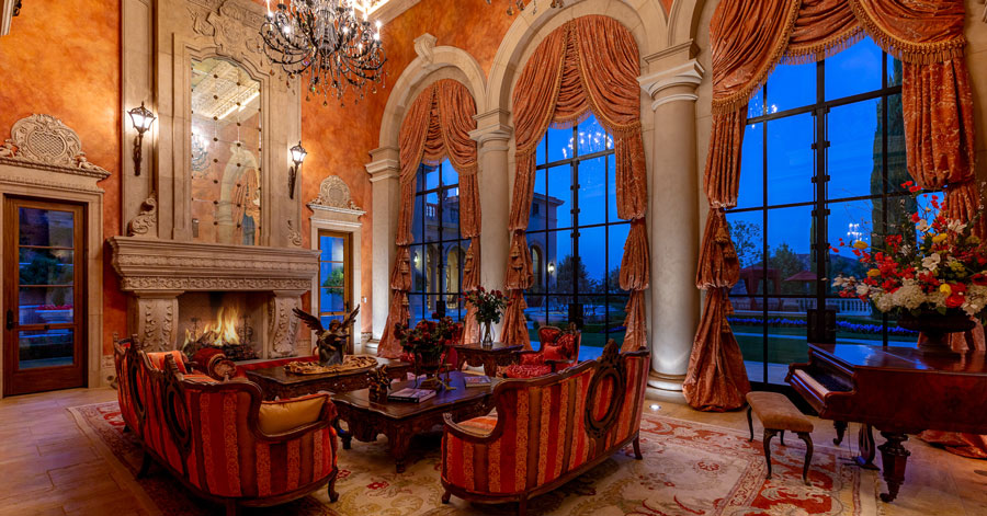 Ornate room with high ceilings and a carved travertine fireplace, crystal chandelier, and luxurious seating area