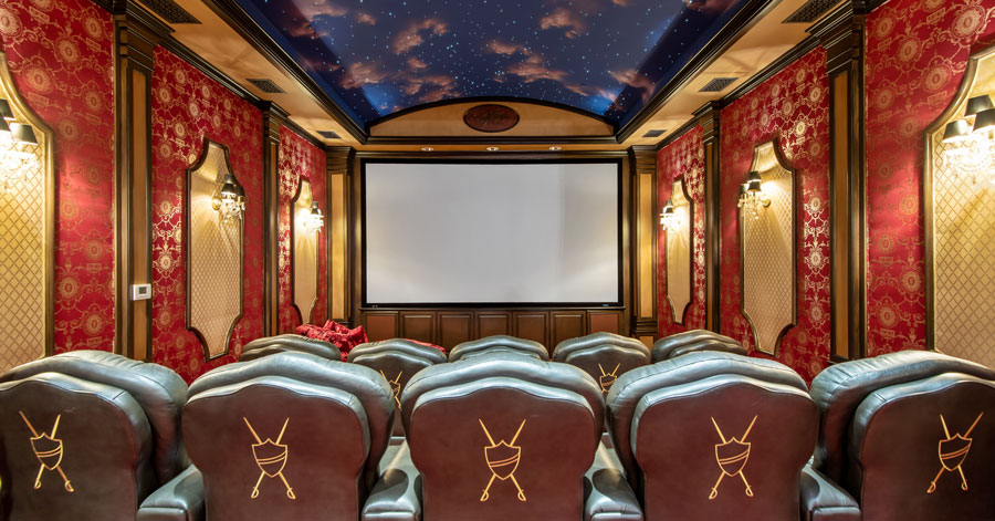 Home theater with red and gold walls, starry night sky wallpaper on ceilings, an brown leather theater seats.