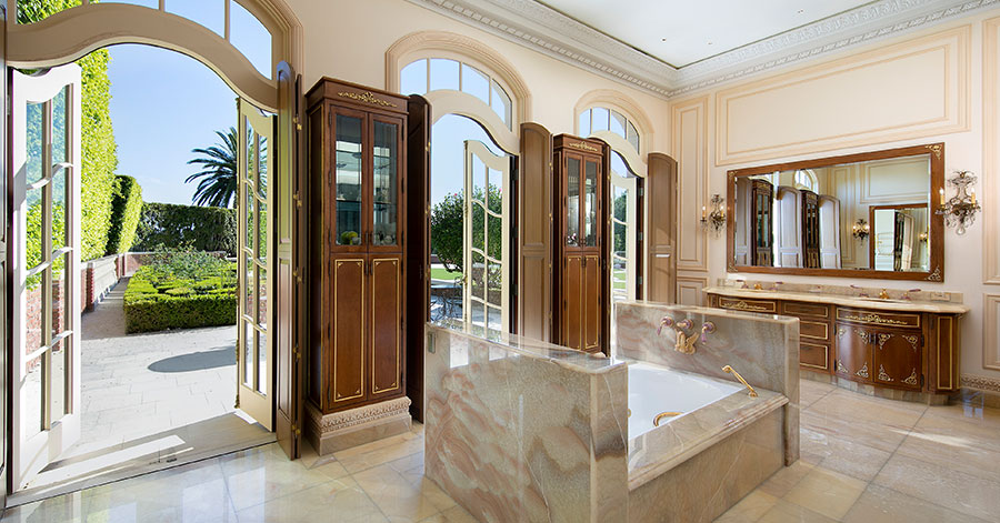 Marbled bathroom with high ceilings, large doors, bright natural light, and gold fixtures on dark brown wood 