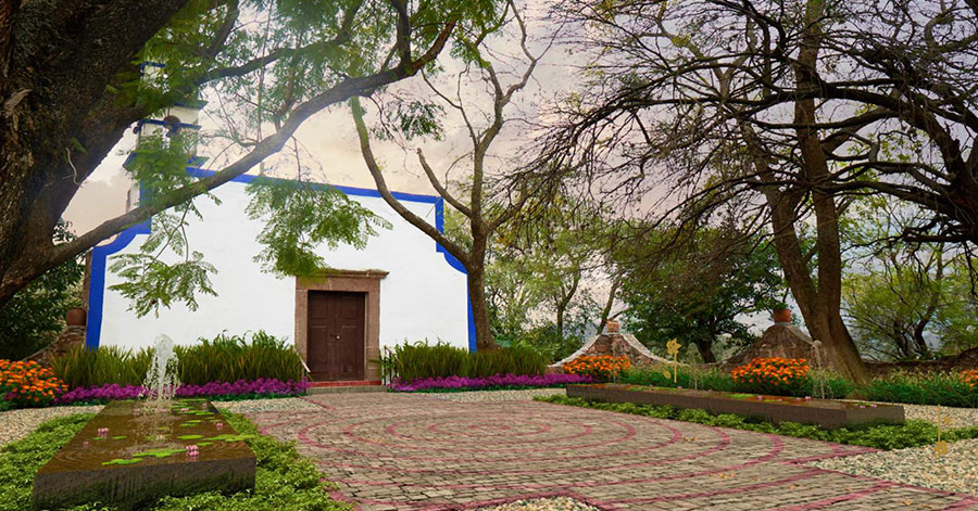 A white hacienda with bright blue trim sitting in front of a stone courtyard covered by trees and filled with colorful flowers