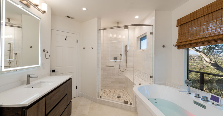 bathroom with soaking bathtub, glass shower, vanity and sink. window with wooded views