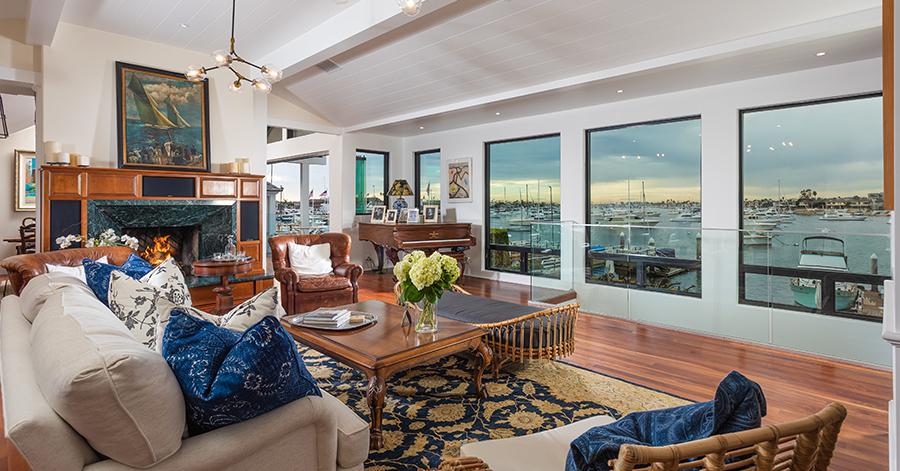 View of Newport Beach home's living room and picture windows showing harbor outside. 