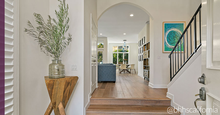 Entry of one of the remodeled homes in Southern California - white walls and two light wood steps lead through arch into living area filled with natural light