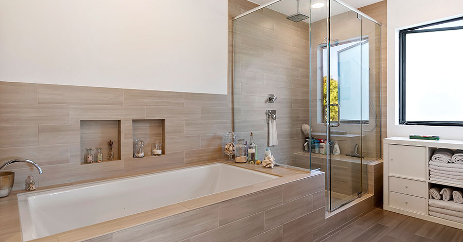 Primary bathroom with glass walled shower, large soaking tub, and luxury brown wood flooring and paneling 