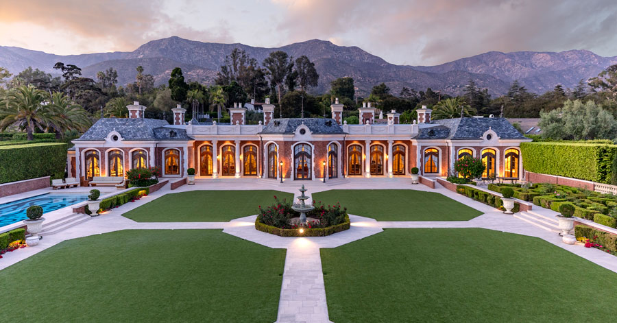 Exterior shot of back of Montecito estate with pristine green lawns, manicured hedge maze, a fountain, and large pool 