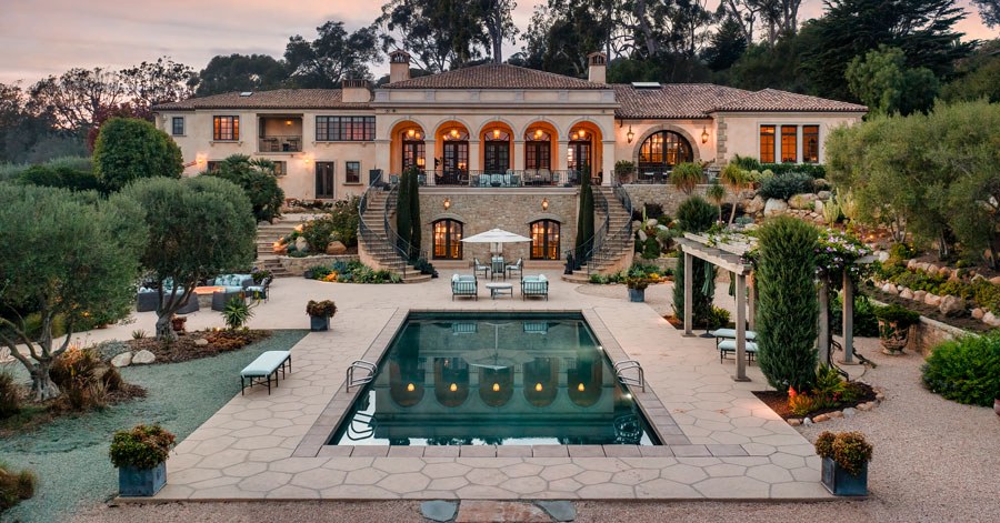 View from pool looking at a Montecito estate with two curved staircases leading from the second floor balcony to the pool area 