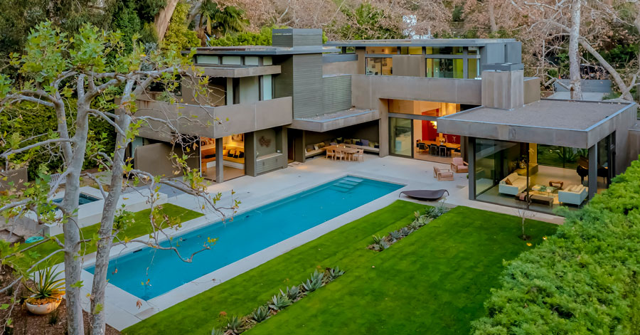 View of modern home with stone and glass walls in Santa Monica with lush green grass and long narrow pool 