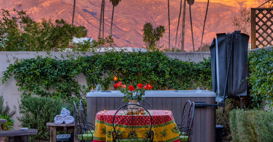 Table for six with colorful tablecloth set in front of a hot tub and lush green vines covering the walled garden 