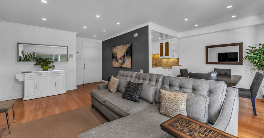 living room in a los angeles condo with dining area and kitchen behind large grey couch 