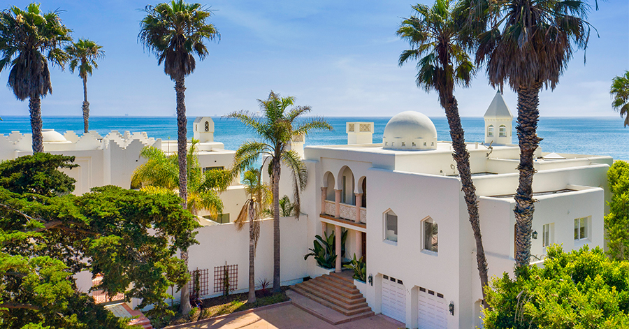 aerial view of spanish style home with white exteriors and blue ocean in the distance 