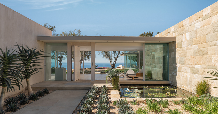 View from exterior of home looking through walls of glass to ocean view beyond 