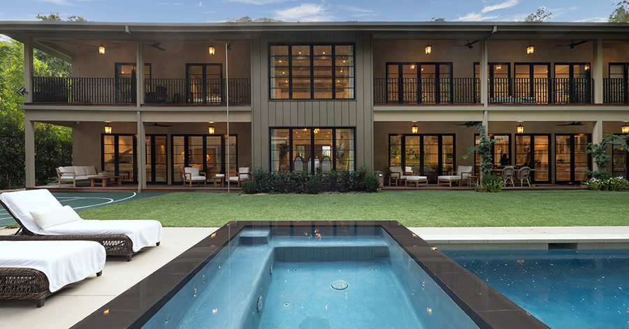 exterior of estate with wood paneled walls and a sparkling pool at dusk 