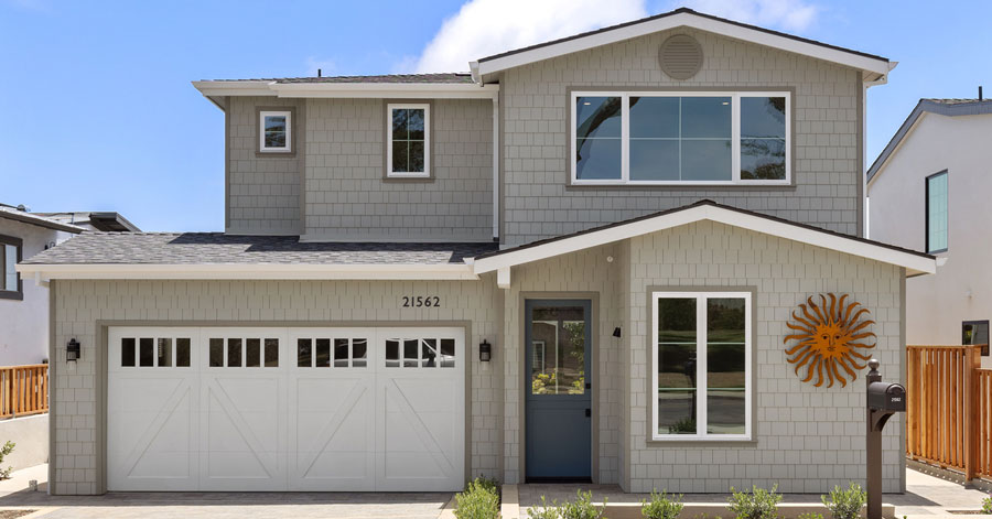 newly constructed laguna beach home with grey shingles exterior, white barn garage door and blue front door