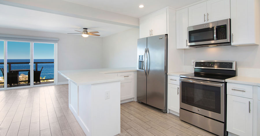 modern white kitchen with stainless steel appliances and blue ocean view beyond second floor balcony 