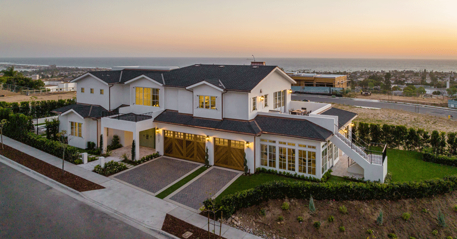 Aerial view of large white two story house with gray roof and ocean in the background