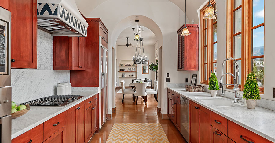 brightly lit kitchen with vibrant red cabinetry, white stone countertops and unique tile on floor and hood of stove