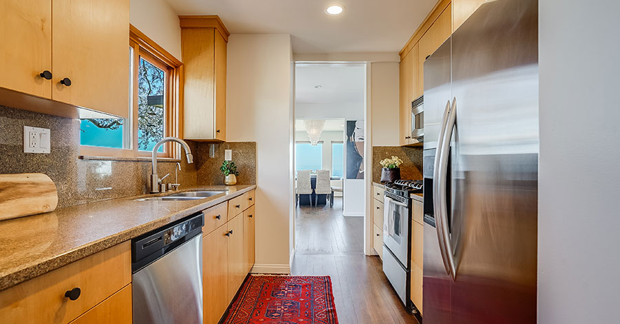 galley style kitchen with light brown cabinets, granite counter tops, and stainless steel appliances 