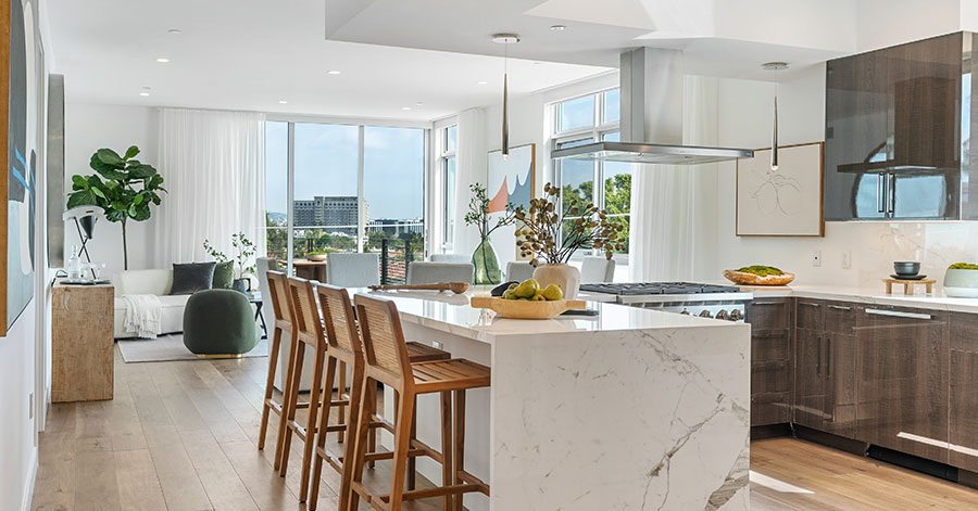 view of kitchen looking out to the outside. white marble waterfall countertops and dark cabinets with stainless steel appliances 